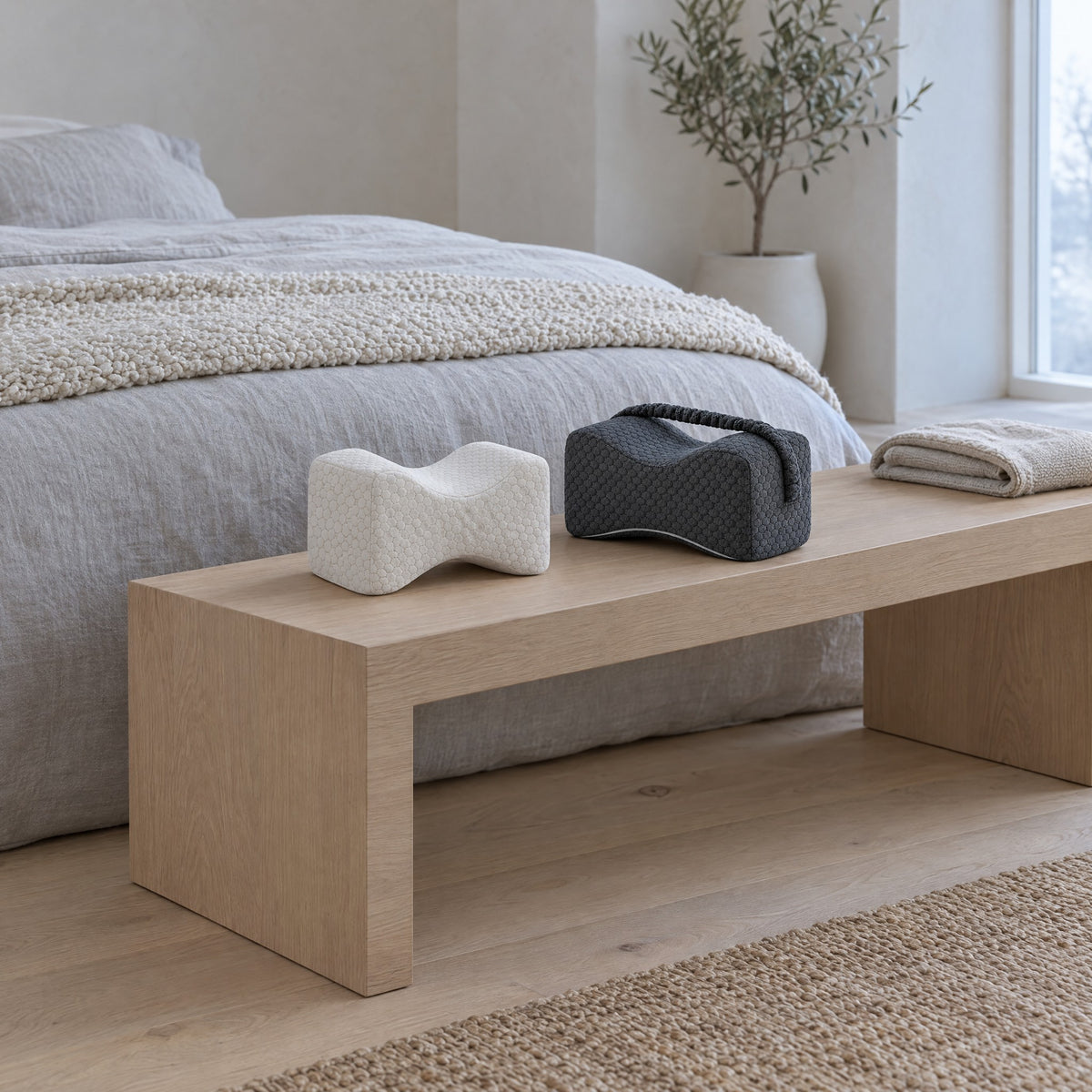 Coussins de jambes GENOU blanc et gris foncé sur un banc en chêne au pied du lit