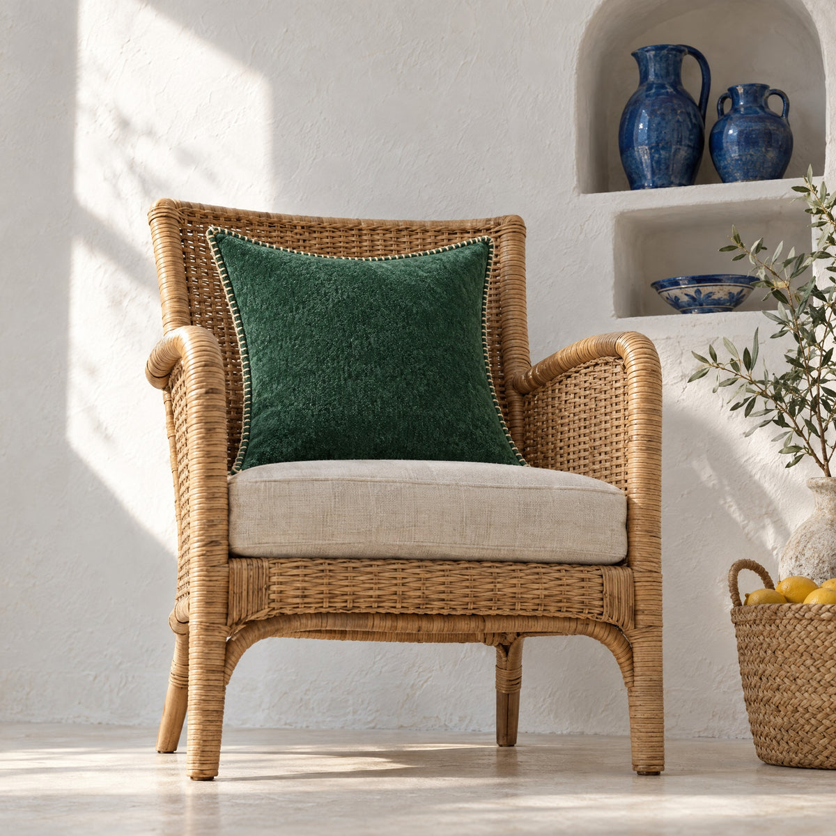 Coussin GALON vert forêt sur un fauteuil en osier, près d'une niche à céramiques bleues