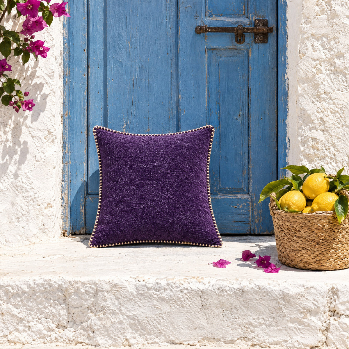 Coussin GALON violet posé sur une marche chaulée devant une porte bleue