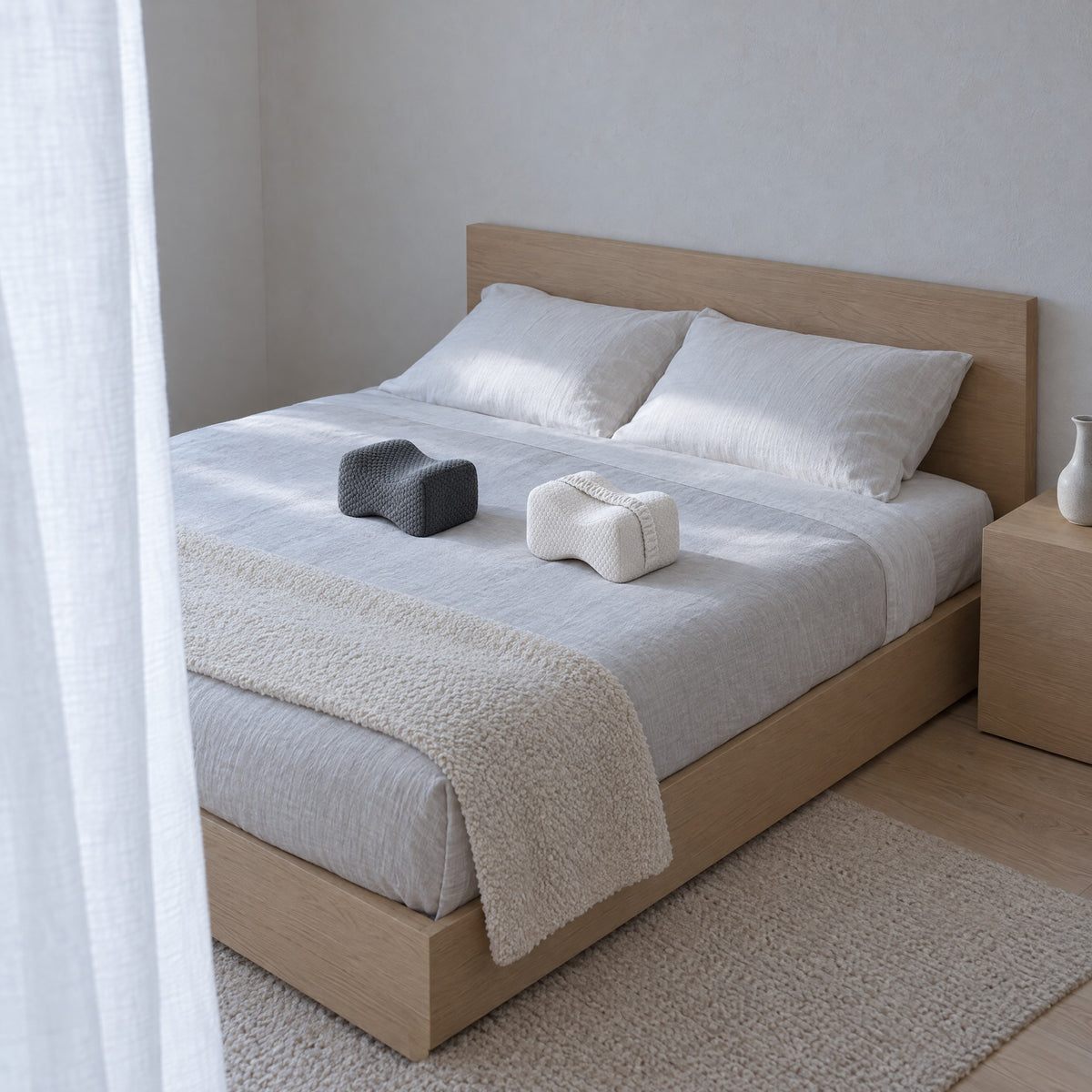 Coussins de jambes GENOU gris foncé et blanc sur un lit en lin, lumière du matin