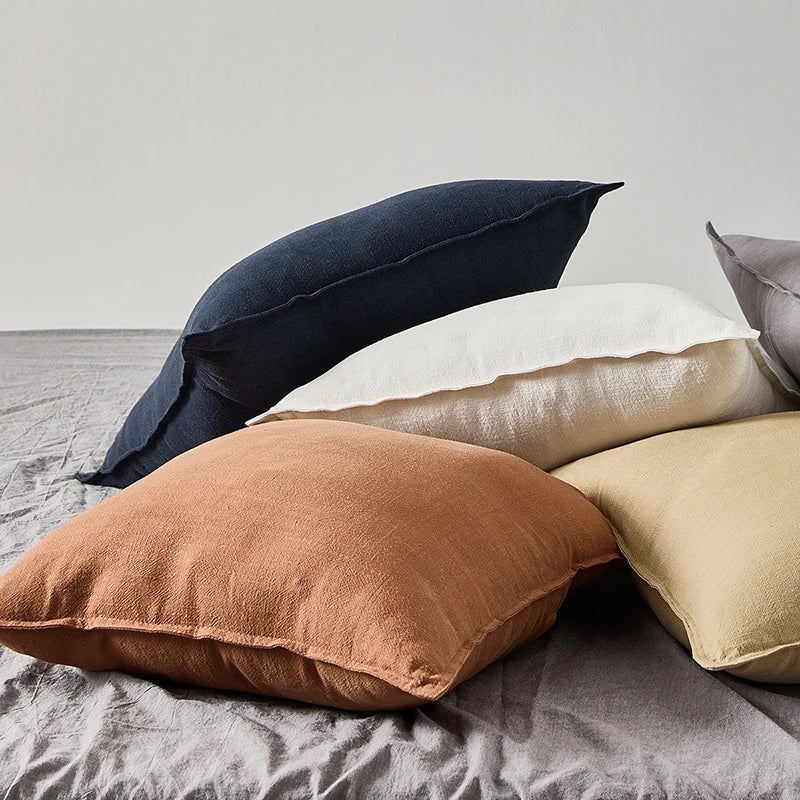 LINETTE — Housses de coussin en coton et lin à bordure plate empilées sur un lit, coloris Bleu marine, Blanc, Terracotta et Ocre