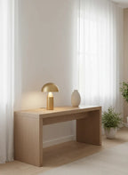 CÈPE — Lampe dorée allumée sur une console en bois clair, ambiance cocon